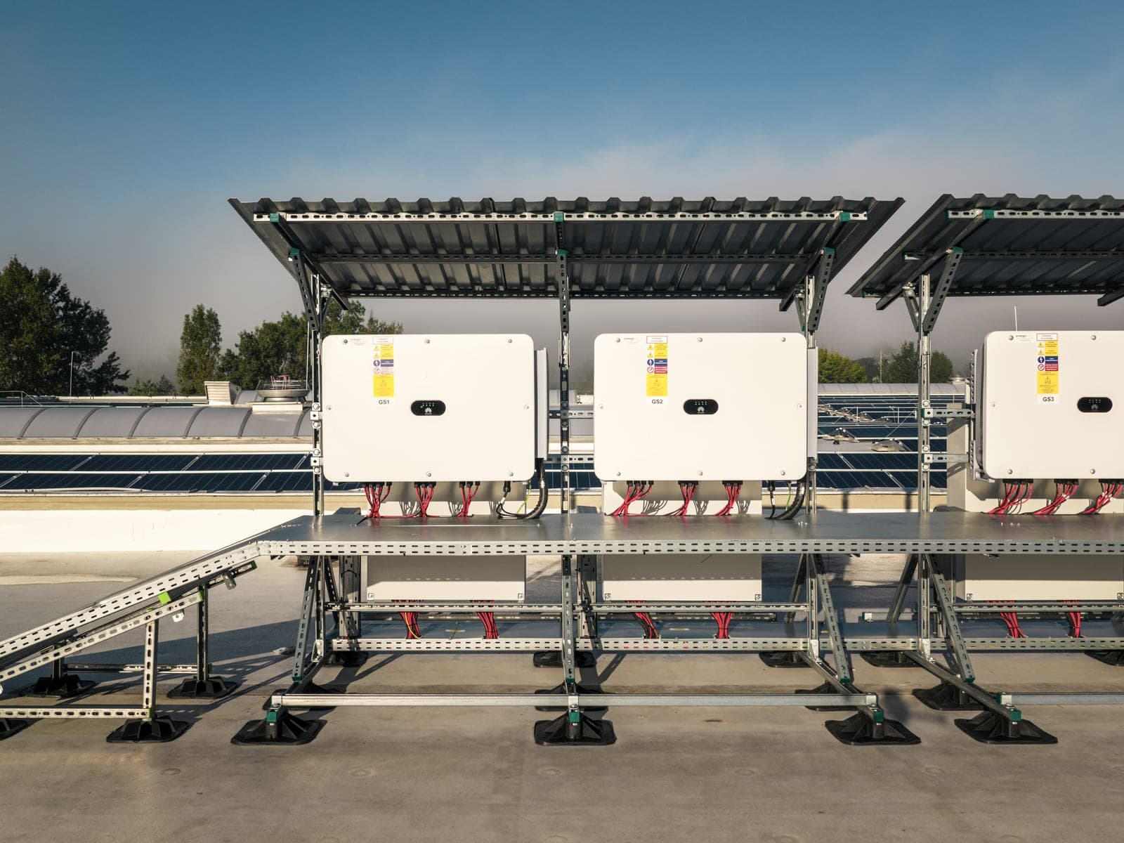String inverters under a canopy on the roof, cabling in trays