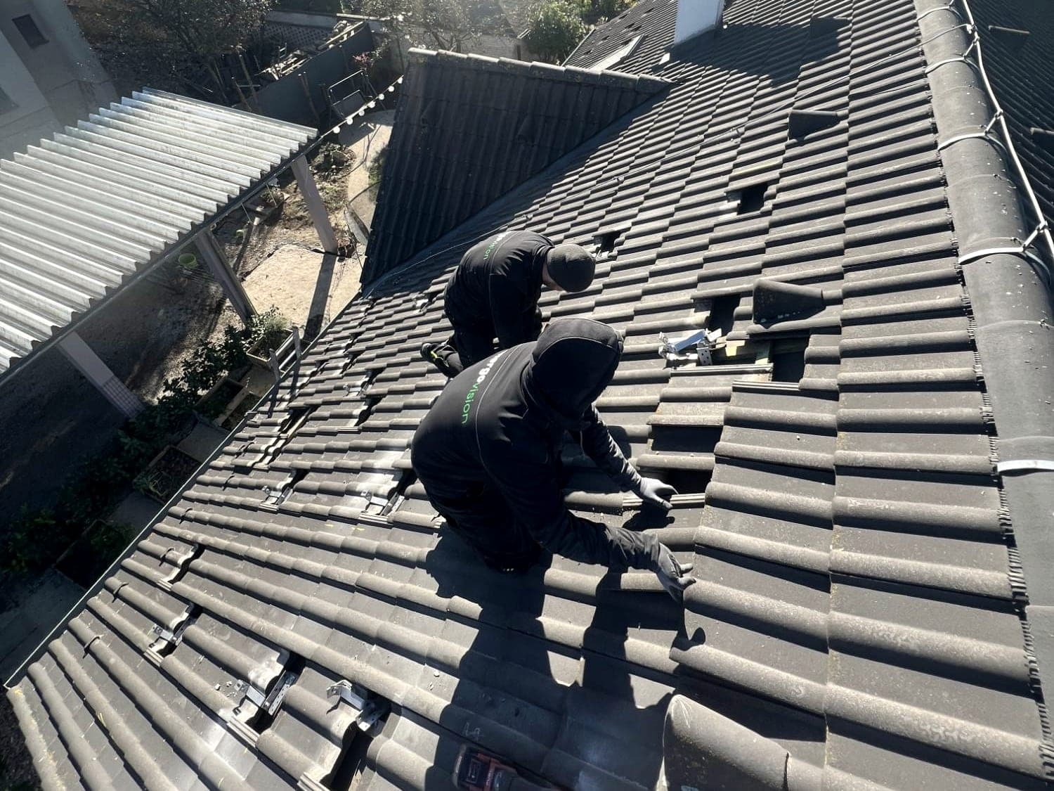 Two Energovision installers fixing roof hooks on the tiled roof of a family house