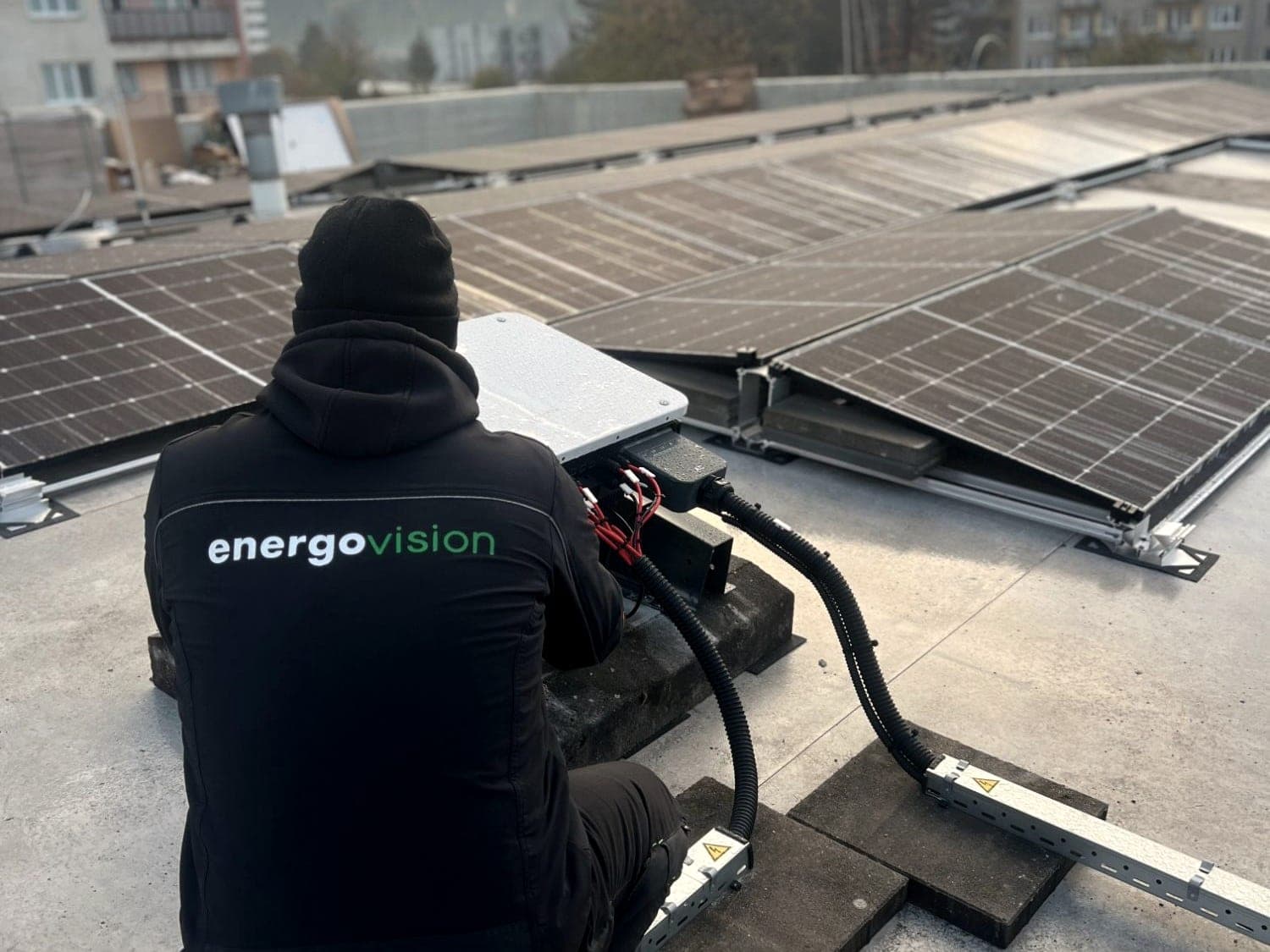 Energovision technician connecting an inverter on a flat roof between rows of panels