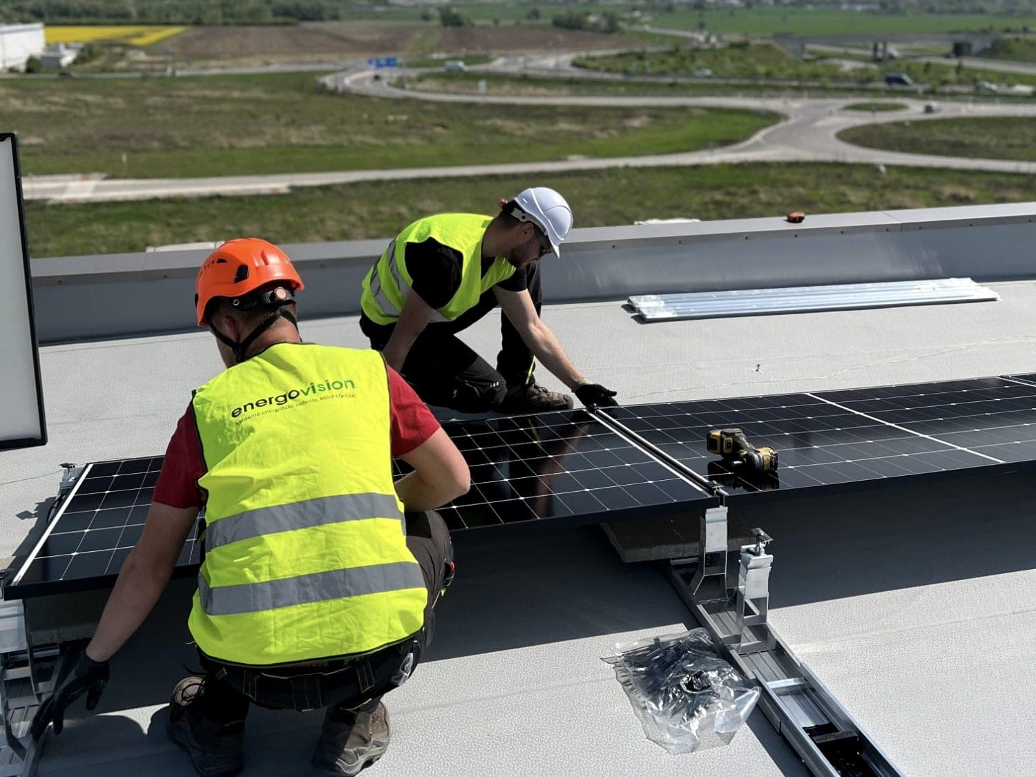 Two installers in high-visibility vests fitting panels on the flat roof of a hall