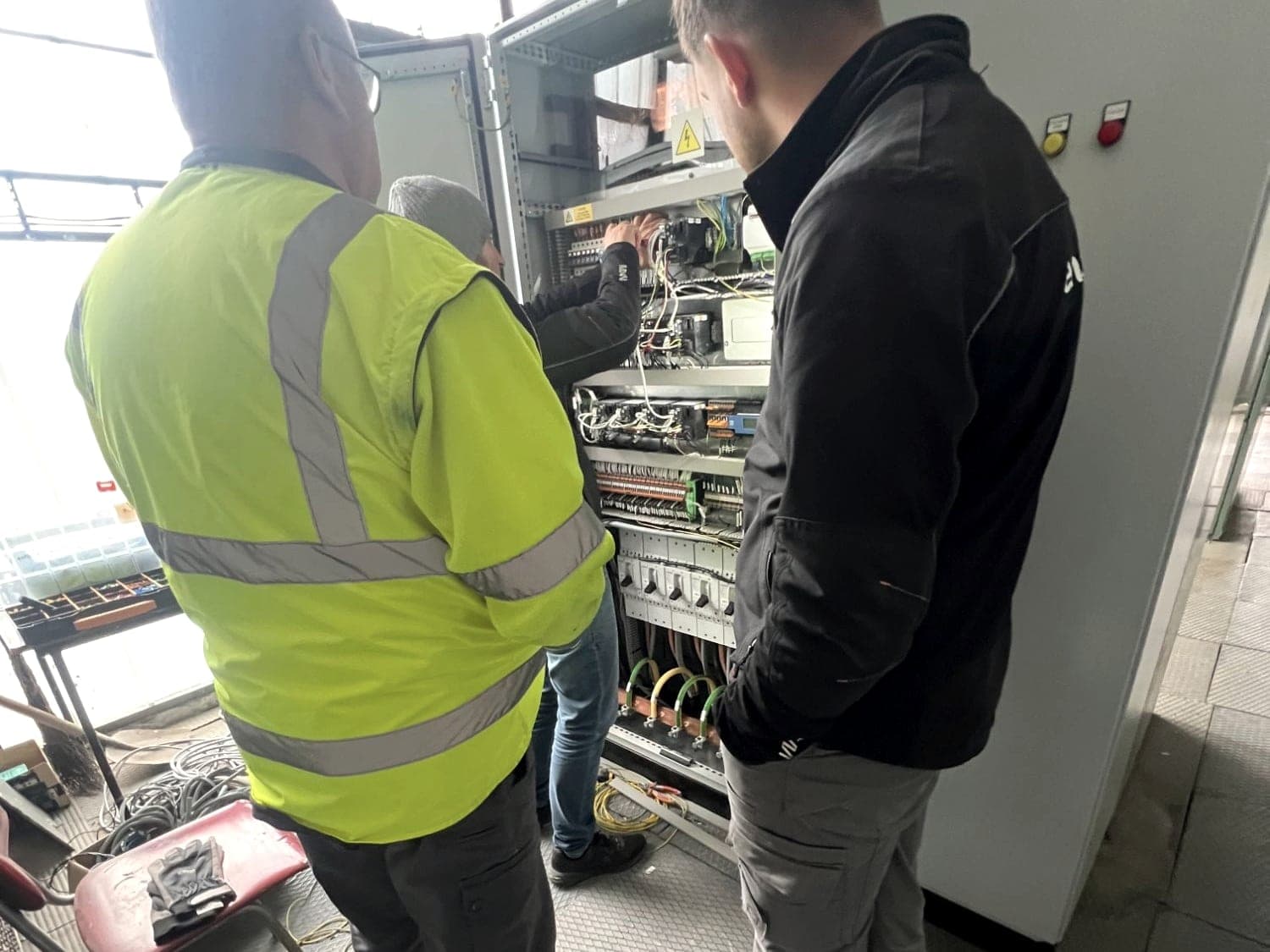 Three technicians at an open control cabinet during a service call