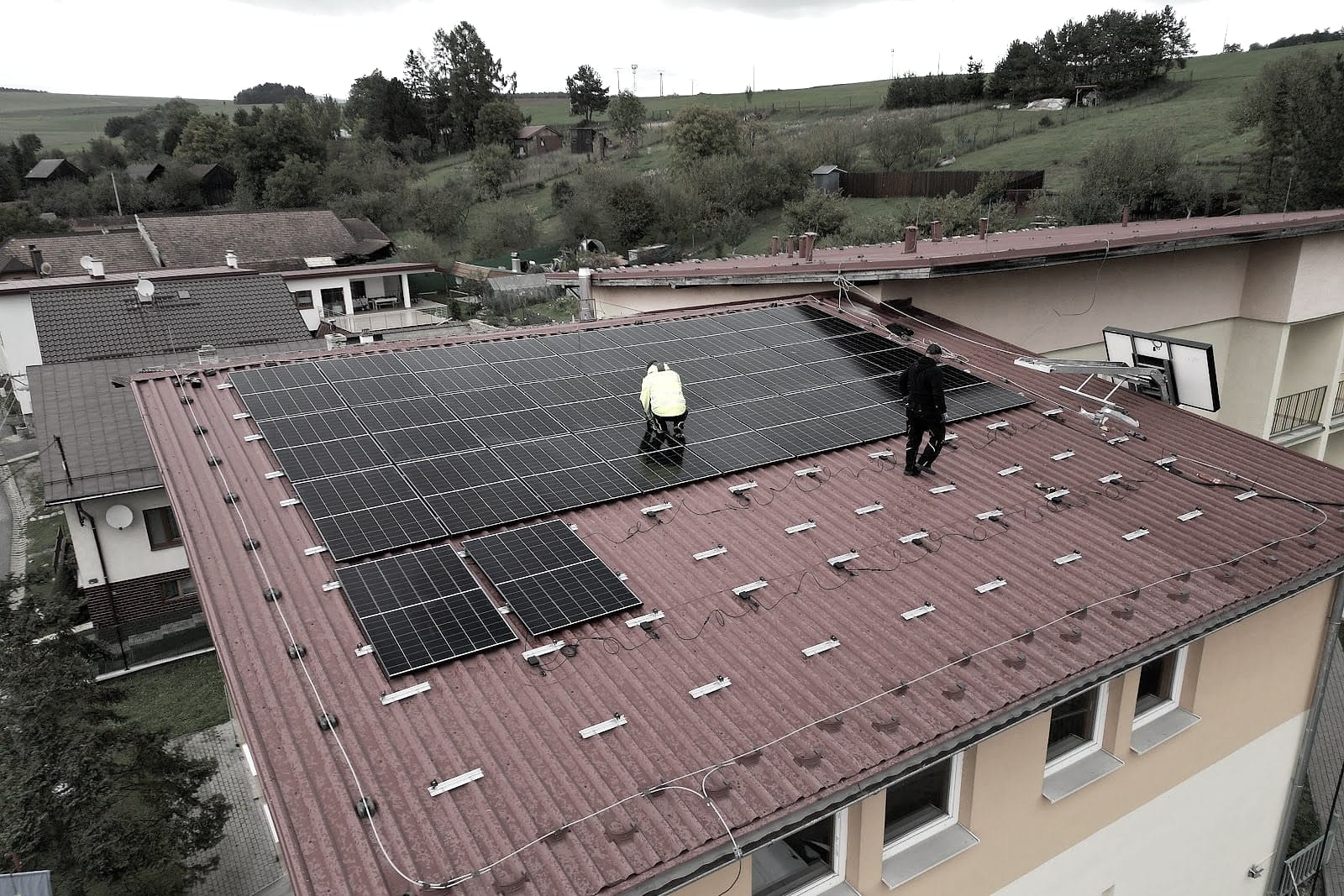 Aerial photo of a family home with a red roof during solar panel installation, installers in high-visibility vests