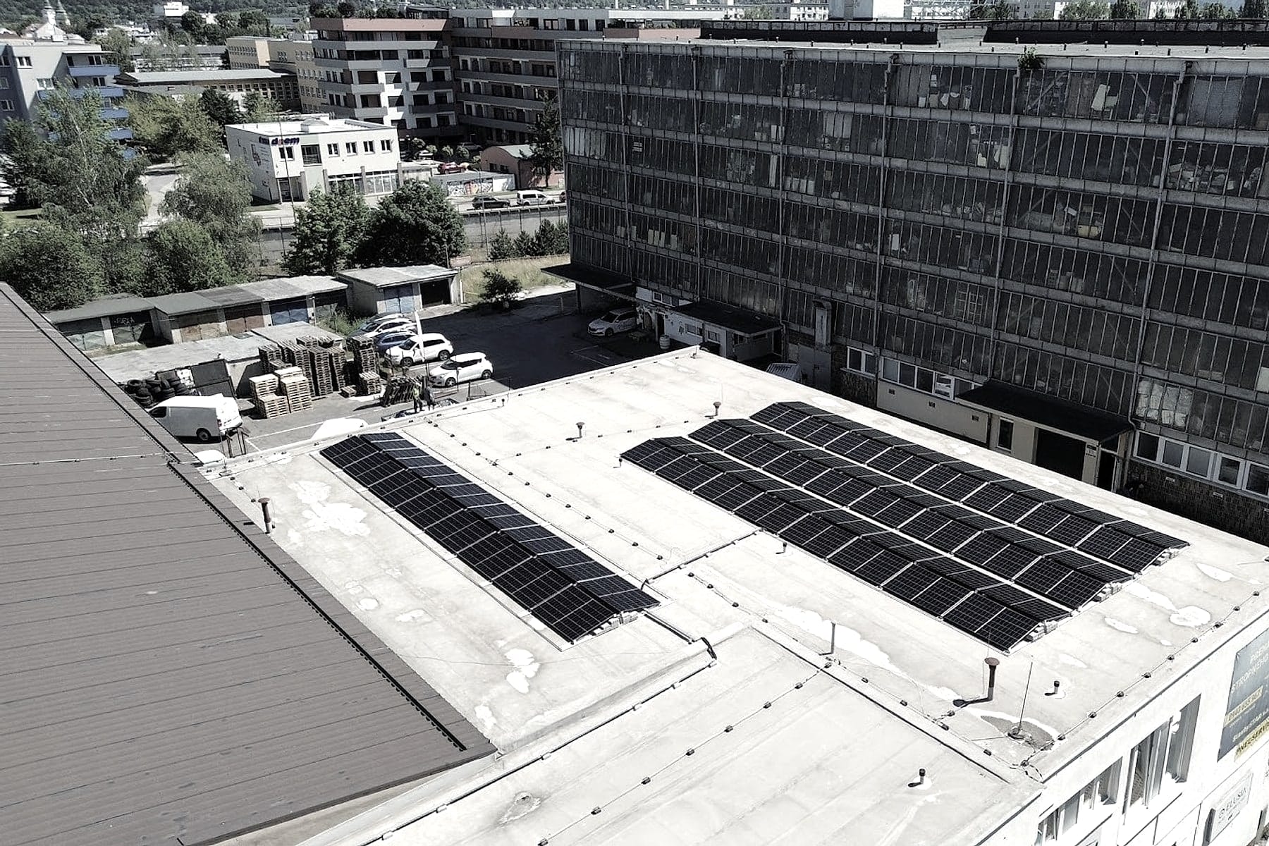 Aerial photo of a flat roof with a solar PV plant in Žilina, a car park and neighbouring buildings
